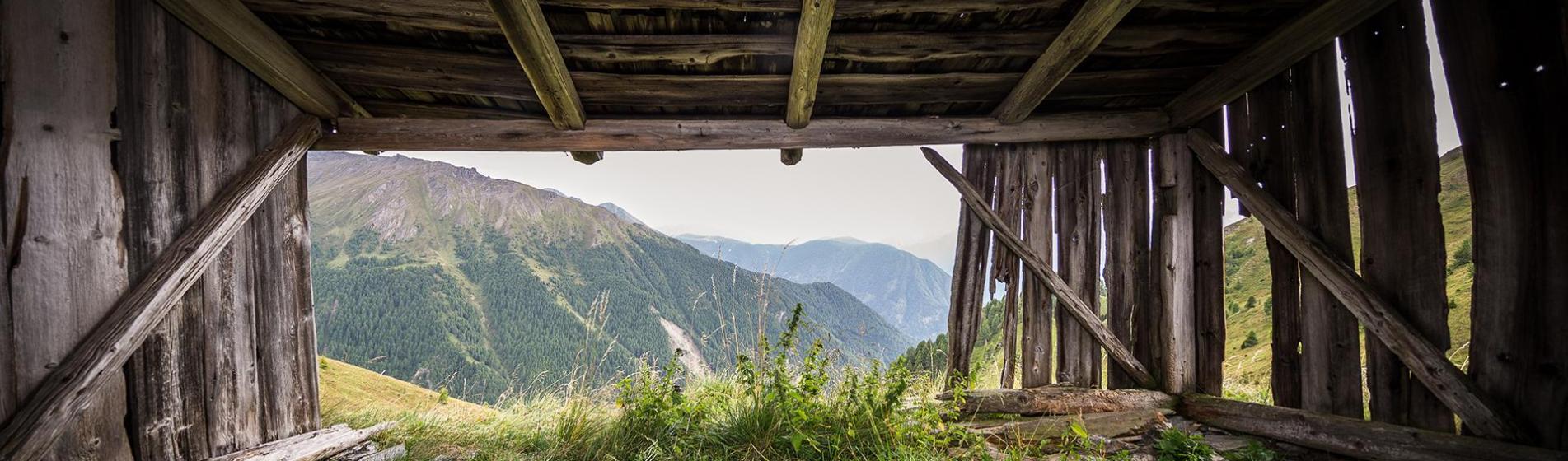 View from an old wooden cabin overlooking a lush mountain landscape with meadows and forests.