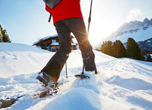 Snowshoer hiking through deep snow in the sunshine, surrounded by alpine winter scenery.