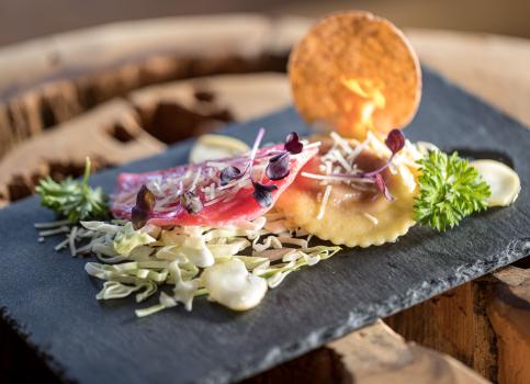 Ravioli finemente impiattati con cavolo rosso, parmigiano e decorazioni su ardesia