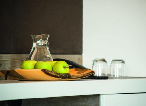 Fresh green apples in a wooden bowl with a water carafe and glasses on a light wooden table.