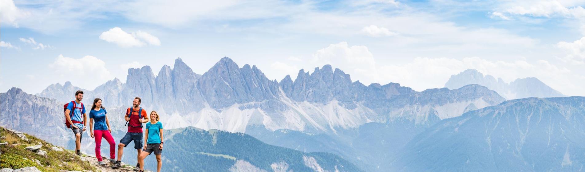 Vier Wanderer auf einem Bergpfad mit weitem Blick auf die Geislergruppe in den Dolomiten.