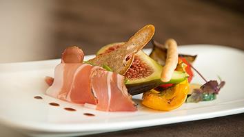 Antipasto raffinato con prosciutto crudo, fichi, verdure grigliate, crostini e gocce di aceto balsamico.