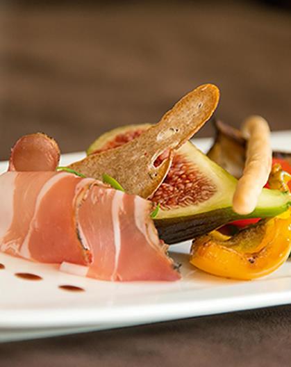 Elegant appetizer with prosciutto, figs, grilled vegetables, crispbread, and balsamic dots.