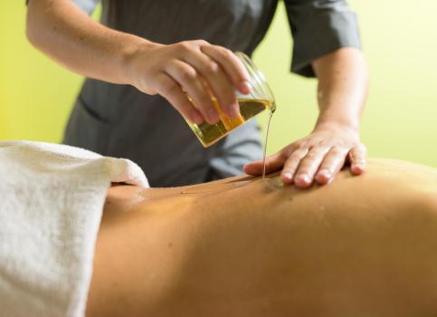 Wellness treatment: therapist pours warm massage oil on the back of a lying person.