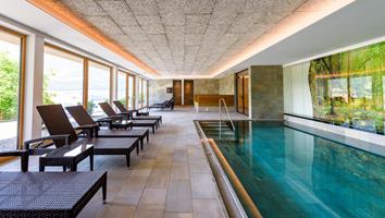 Heller Indoorpool mit Liegen und Waldbild an der Wand