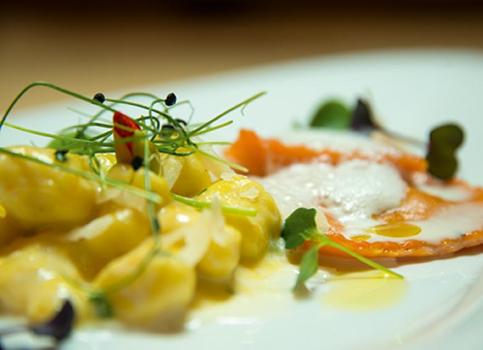 Gnocchi con salsa gialla e ravioli rossi con schiuma, guarniti con germogli