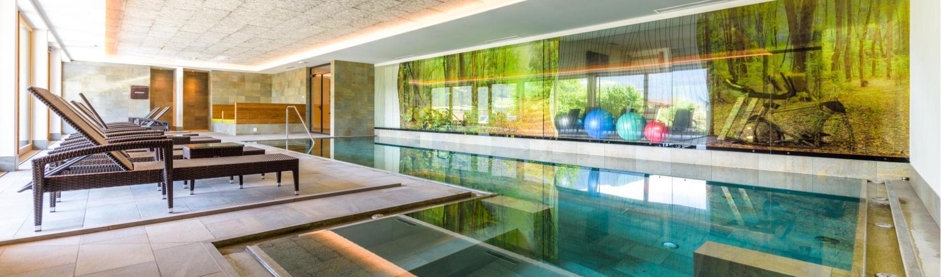 Piscina interna luminosa con lettini e un'immagine del bosco