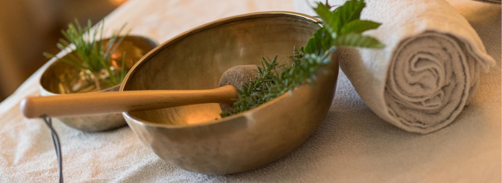 Singing bowls with herbs and two rolled towels on a massage table in the spa area.