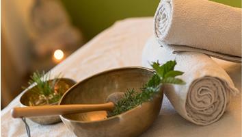 Campane tibetane con erbe e due asciugamani arrotolati su un lettino da massaggio nella spa.