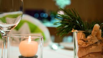Close-up of a festive table setting with candle, wine glass, and pine branch decoration in glass.
