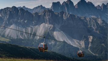 Due cabine sospese davanti allo spettacolare sfondo delle Dolomiti sopra pascoli verdi.
