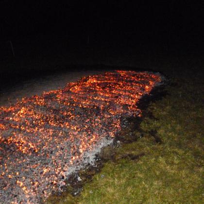 Leuchtendes Glutbett auf einer Wiese bei Nacht, vorbereitet für einen traditionellen Feuerlauf.