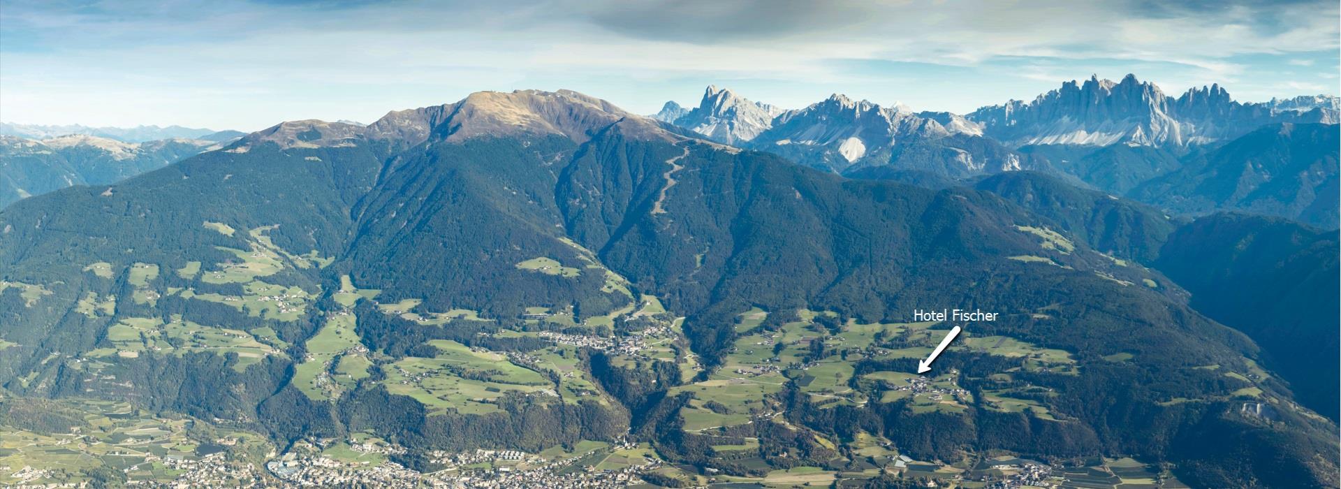 Panoramablick auf das grüne Eisacktal in Südtirol mit dem eingezeichneten Standort des Hotel Fischer vor der beeindruckenden Kulisse der Dolomiten.