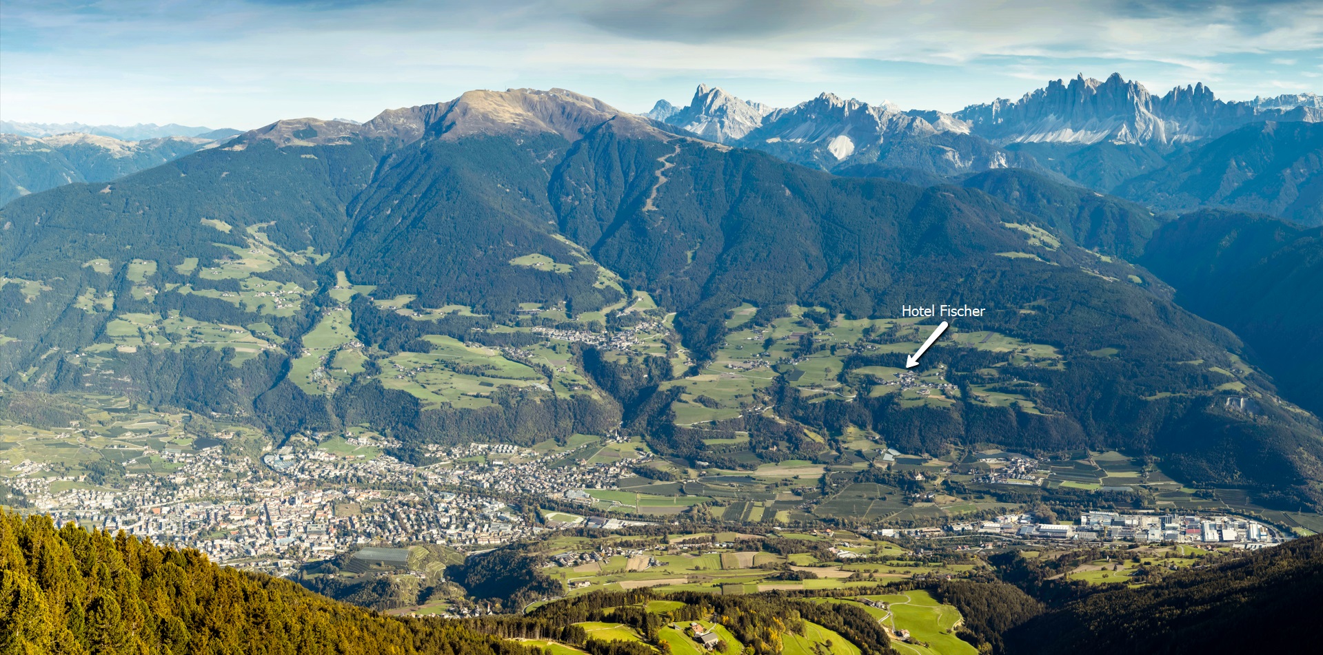 Panoramablick auf das grüne Eisacktal in Südtirol mit dem eingezeichneten Standort des Hotel Fischer vor der beeindruckenden Kulisse der Dolomiten.