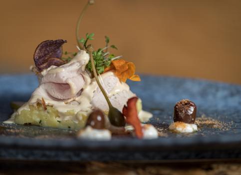 Vitello finemente impiattato con cappero, chips di radici, crescione e olive.