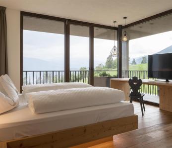 Camera luminosa con letto grande, TV e finestre panoramiche con vista sul paesaggio verde.