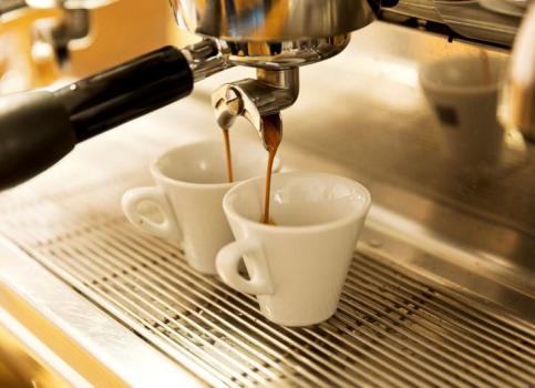 Two freshly brewed espressos pour into white cups from a portafilter machine.