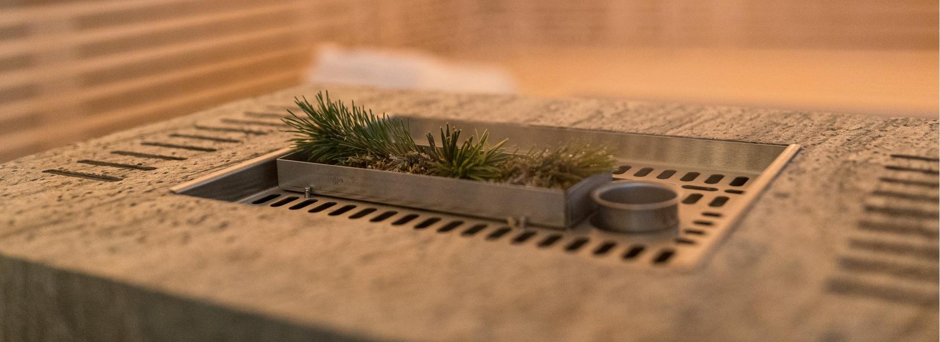 Sauna con stufa in pietra moderna, sopra un vassoio metallico con rami freschi di pino.