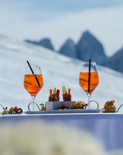 Aperitif and snacks on a white table with snowy mountain peaks in the background.