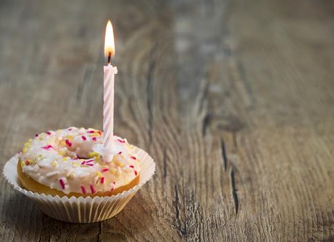 Donut with icing and sprinkles, topped with a lit birthday candle