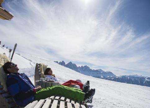 Zwei Skifahrer entspannen in Liegestühlen im Schnee mit Blick auf die Dolomiten in der Sonne.