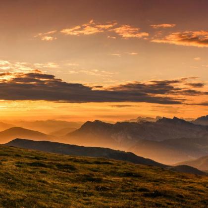 Wanderer auf einer Wiese vor spektakulärem Alpenpanorama bei Sonnenuntergang.