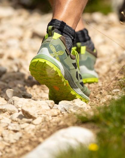 Close-up of hiking shoes on a rocky mountain trail with grass and wildflowers along the edge.