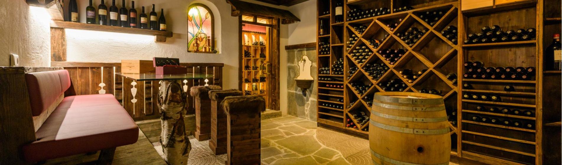 Cantina accogliente con scaffali in legno, barrique, zona salotto e pavimento in pietra rustica.