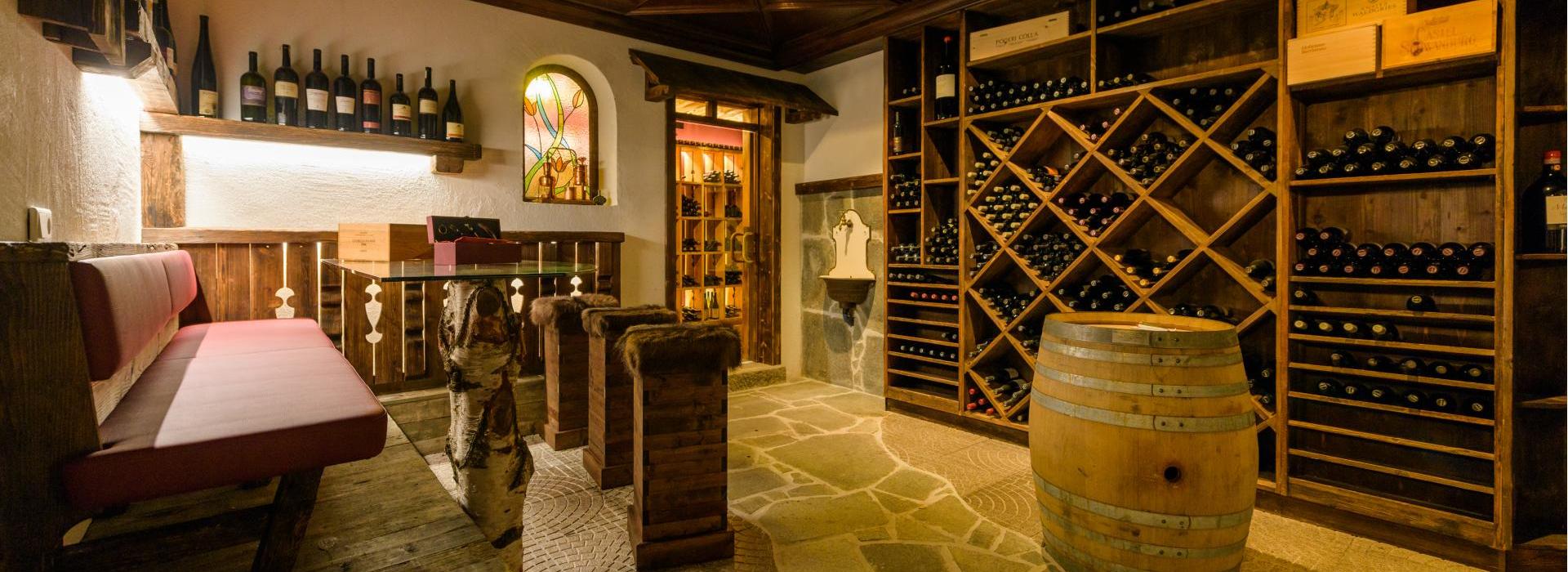 Cantina accogliente con scaffali in legno, barrique, zona salotto e pavimento in pietra rustica.