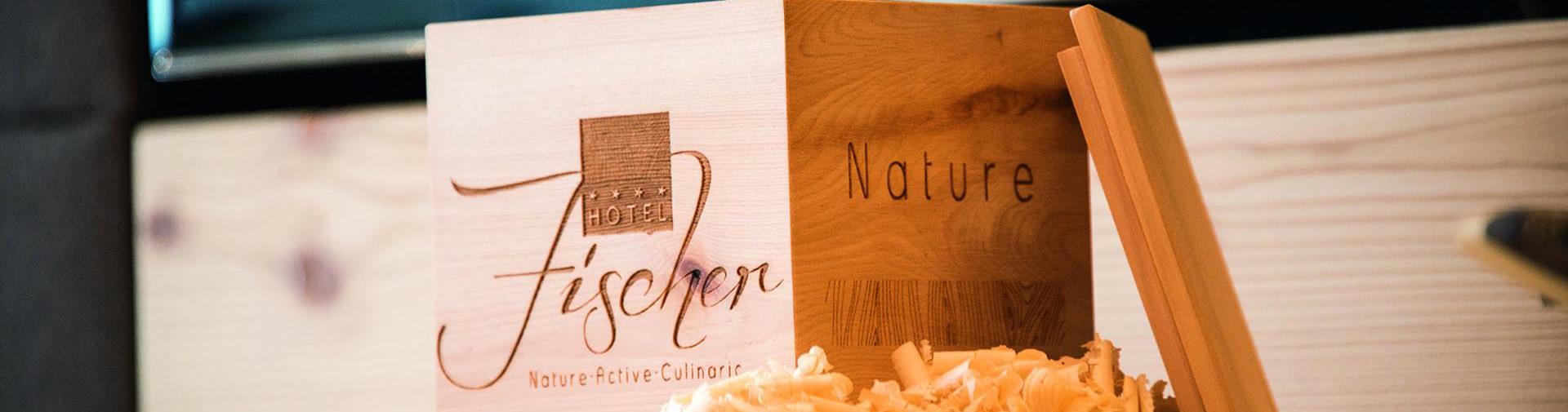 Wooden box with “Hotel Fischer” logo and wood shavings, beside a lid labeled “Nature”.