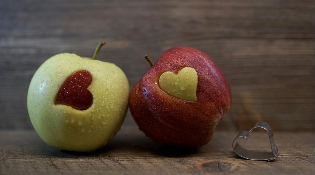 Due mele con cuori intagliati a colori invertiti, accanto una formina a forma di cuore.