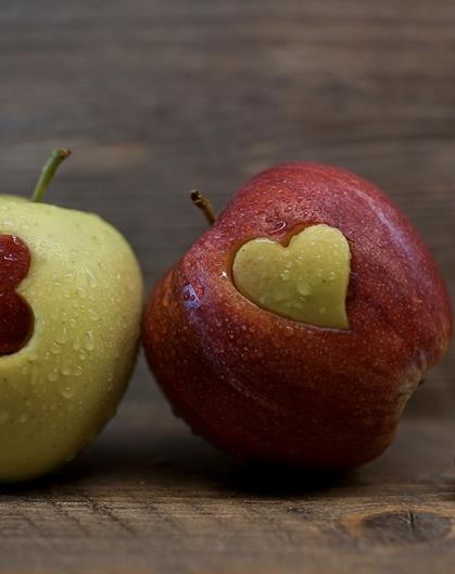 Two apples with heart-shaped cutouts in reversed colors, next to a heart-shaped cookie cutter.