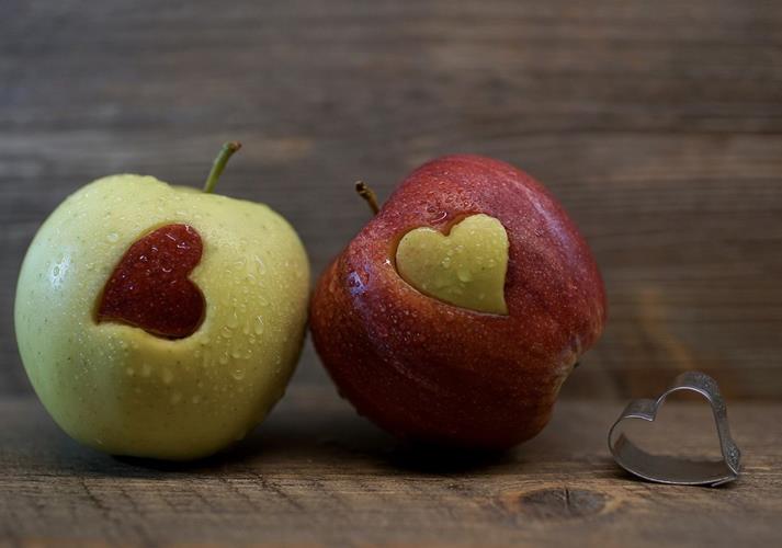Two apples with heart-shaped cutouts in reversed colors, next to a heart-shaped cookie cutter.