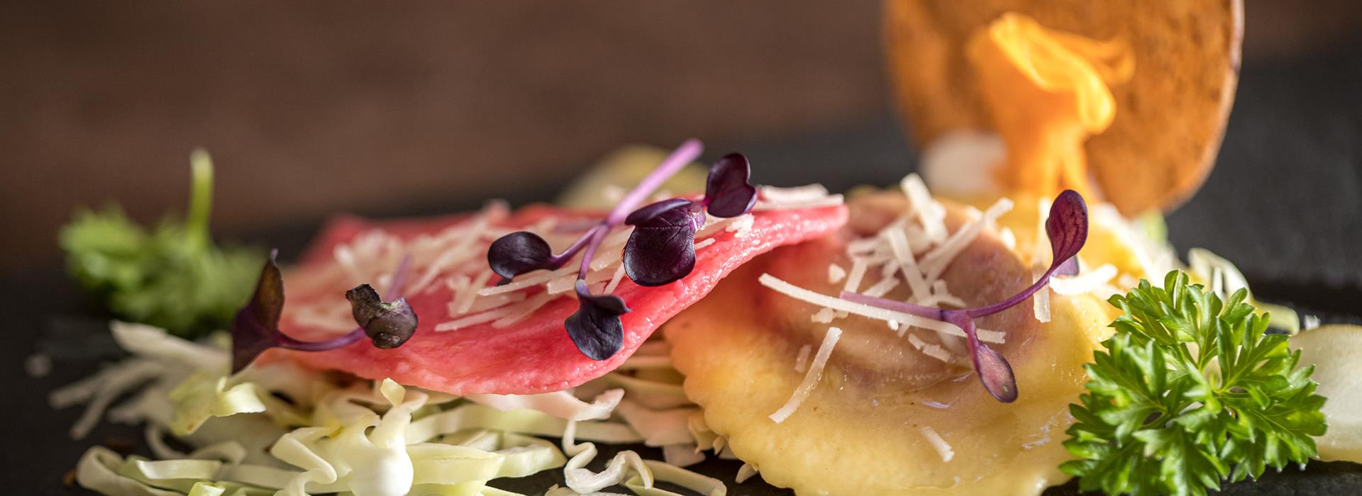 Finely plated ravioli with red cabbage, parmesan, and garnish on a slate
