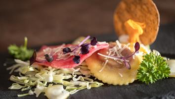 Finely plated ravioli with red cabbage, parmesan, and garnish on a slate