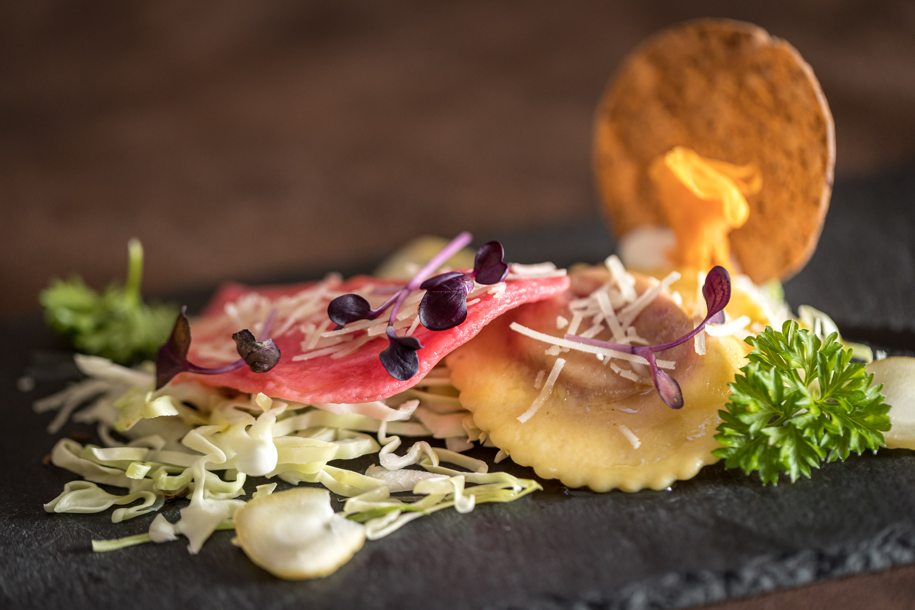 Fein angerichtete Ravioli mit Rotkraut, Parmesan und Deko auf Schieferplatte