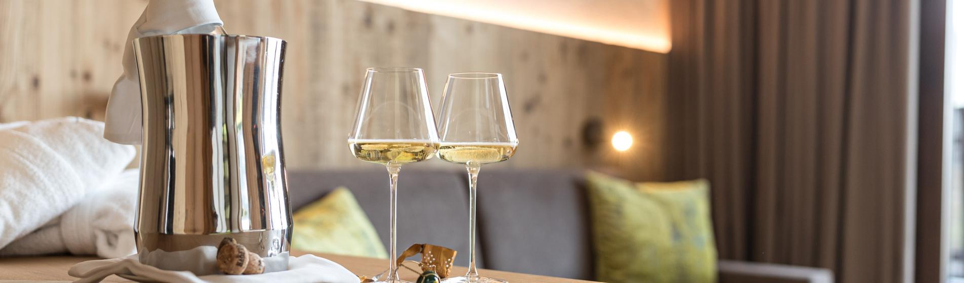 Due calici di vino bianco con bottiglia fresca su un tavolo in legno in una delle nostre suite