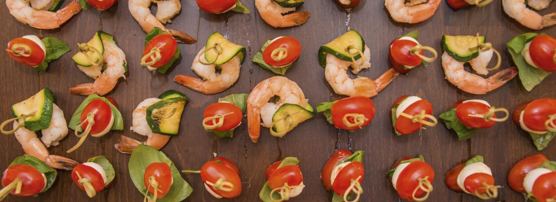 Colorful appetizers with shrimp, zucchini, tomatoes, mozzarella and basil arranged on a wooden tray.