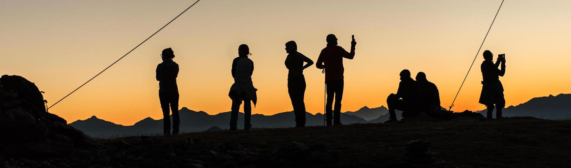 Silhouetten von Wanderern bei Sonnenuntergang auf einem Berggipfel mit Panoramablick.