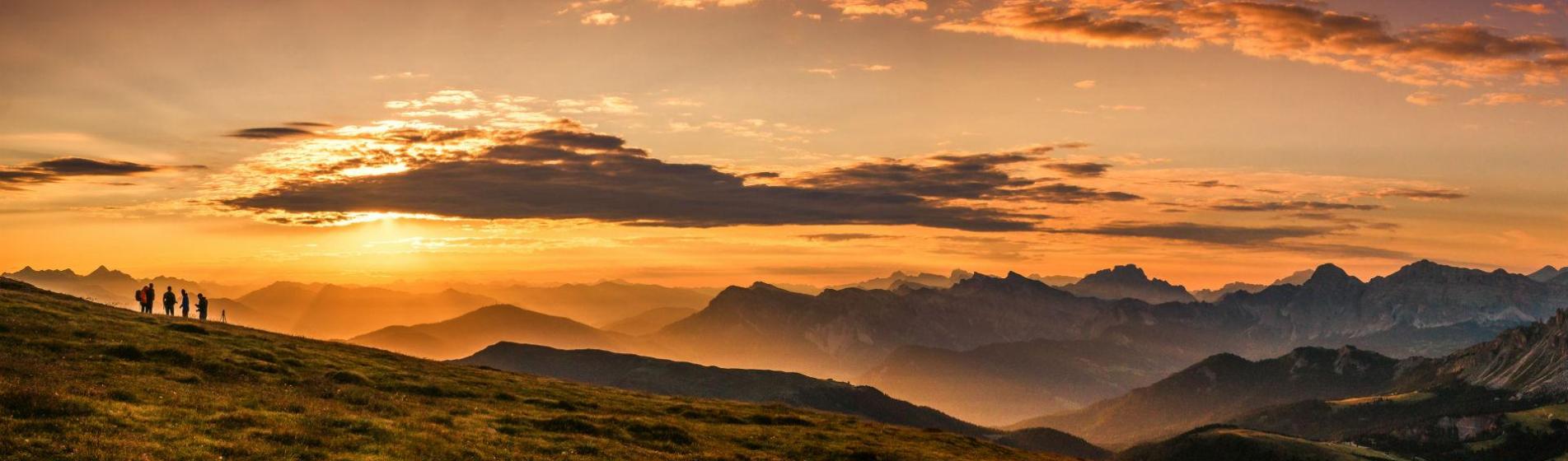 Hikers on a meadow with a stunning Alpine panorama at sunset.