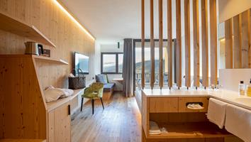 Bright hotel room with wooden furniture, modern sink area, cozy sitting corner and mountain view